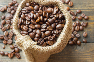 Coffee beans in coffee bag made from burlap on wooden surface. Focused in middle of the frame.