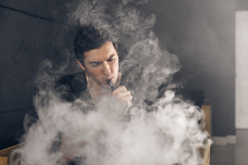 Vaping man holding a mod. A cloud of vapor. Black background. Smoking electronic cigarette Vape advertisement concept