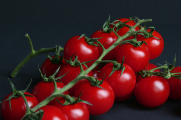 Czerwone, dojrzałe pomidory koktajlowe na gałązce na czarnym tle