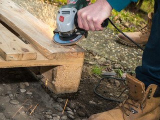 Man sanding a wooden palette, with flying sparks