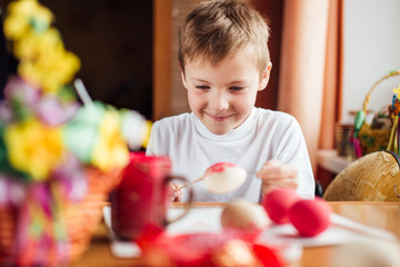 Fototapeta premium Young boy drawing easter eggs at home and smile