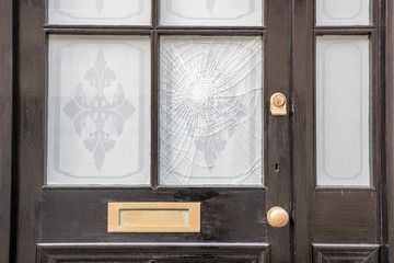 A smashed window pane on a black wooden front door