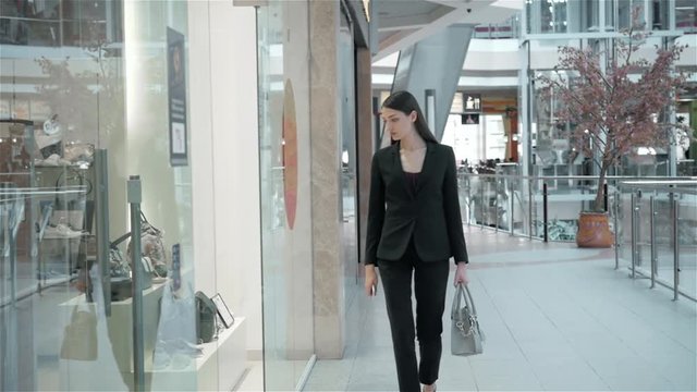 Beautiful young woman looking in a shop window with clothes and dresses and luxury juwellery in shopping mall, business woman in suit shopping