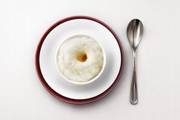 Rice porridge with milk and butter in a white bowl on a white background for breakfast.