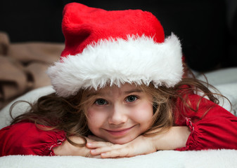 Girl with blonde hair in disguise of Santa Claus in a white-fur cap with a beard resting on his hands