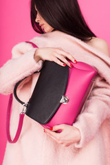 Colored photo in a pink colors - brunette young woman in coat holding handbag with two hands