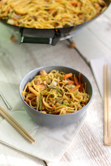Noodles with chicken and various vegetables, prepared in wok. Served on white rustic table. Selective focus.
