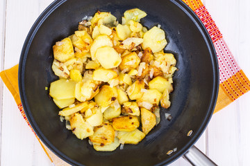 Sliced potatoes fried with onions in frying pan on wooden backgr