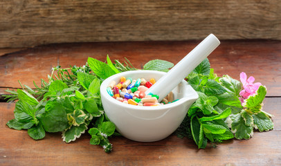 Herbs and pills in a mortar on wooden background