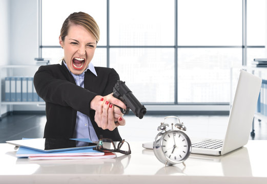 business woman furious and angry working with computer laptop pointing gun to alarm clock