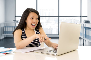 Fototapeta premium happy chinese asian woman working and studying on her computer sitting at modern office desk smiling cheerful