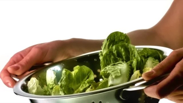 femme qui essore de la salade dans une passoire en inox sur fond blanc en slow motion gros plan
