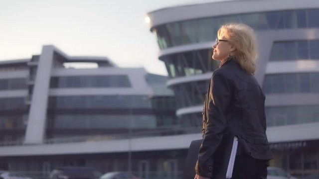 A woman walks down the street towards the sun and holds a folder for documents in her hand. Slow-motion