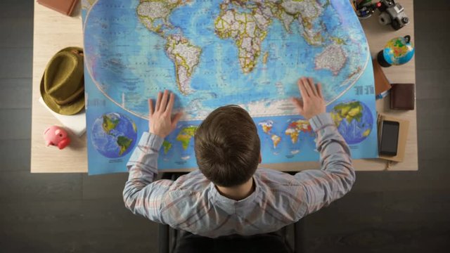 Male unfolding world map to choose country for travel destination, vacation