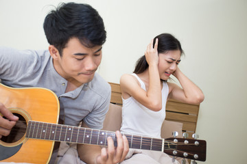 Asian woman annoyed at a man who is singing and playing a guitar.