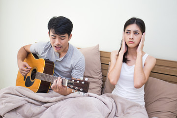 Asian woman annoyed at a man who is singing and playing a guitar.