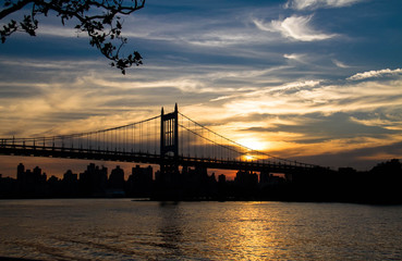 Silhouette of Triborough bridge over the river and city with sunset sky, New York