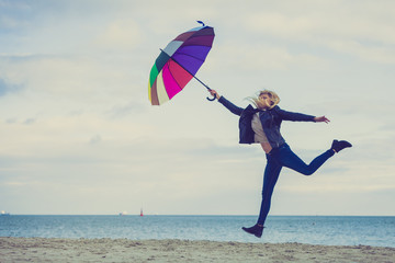 Woman jumping with colorful umbrella on beach
