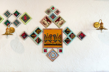 Lamps and folk patterns in frames on a white wall.
