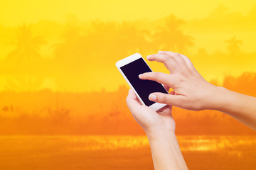 woman hand hold and touch screen smart phone on abstract blurred of nature sunset background.