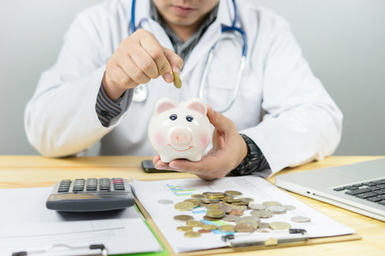 Doctor holding out your piggy bank wanting payment/ Your Savings To Pay Bill, insert coins to it,Stethoscope financial checkup or saving for medical insurance costs money plan fee  Lifestyle concept