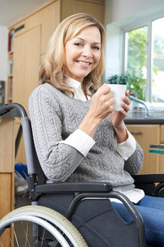 Disabled Woman Sitting In Wheelchair At Home With Hot Drink
