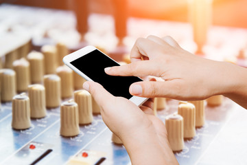 woman hand hold and touch screen smart phone on mixing console background.