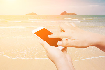 Woman hand hold and touch screen smart phone on the beach and tropical sea