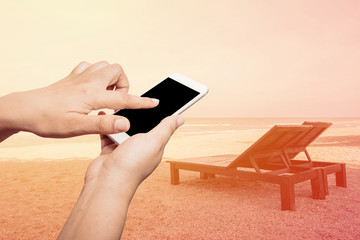 Woman hand hold and touch screen smart phone on the beach and tropical sea
