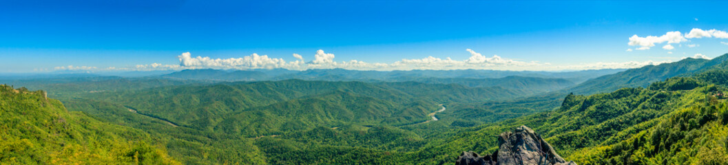 Panorama view of hills and mountain range full of green tree with river through valley and clear blue sky.