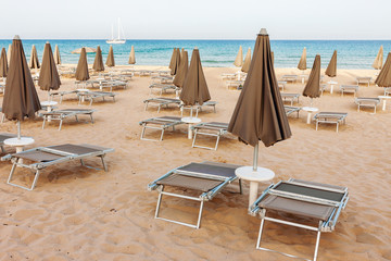 Empty beach, loungers and closed parasols with ocean and lonely yacht in the background