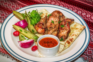 Grilled pork served on flatbread with red onion, pickled cucumbers, dill, parsley and sauce on a plate