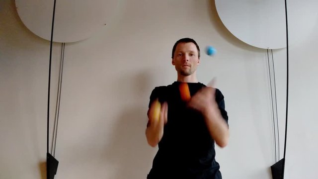 Juggler with three color balls before white wall with decoration on sides