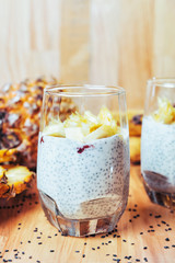 Glasses of chia seeds pudding with mango. Basil seeds in coconut milk with sliced pineapple and banana on a wooden table. A banch of bananas