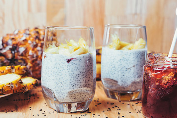 Glasses of chia seeds pudding with mango. Basil seeds in coconut milk with sliced pineapple and banana on a wooden table. A banch of bananas and strawberry jam