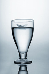 Wine glass with water and origami paper boat concept