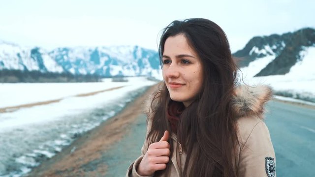 Young beautiful model posing over winter mountains. Stylish fashion portrait. Outdoor winter portrait of young brunette over snowy background. The concept of travel and adventure. Hipster style