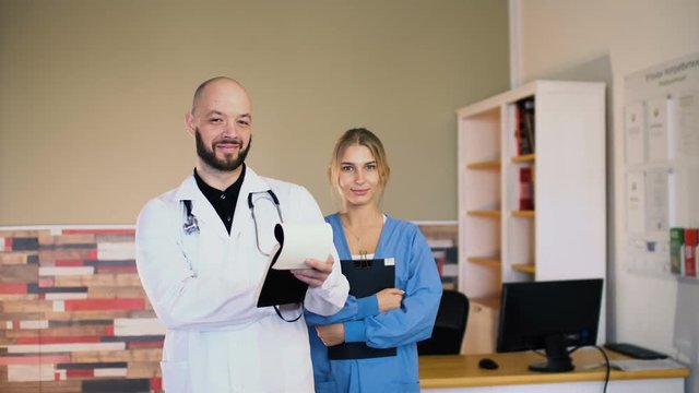 Adult 30s male doctor man with a 20s female nurse in uniform are posing at medical office 4k