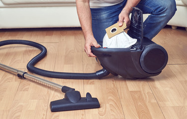 Man taking out a full dust bag from a vacuum cleaner    - obrazy, fototapety, plakaty