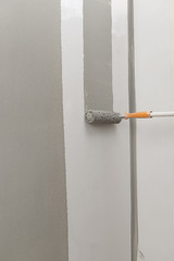 Vertical image of a painting roller painting wall in gray.