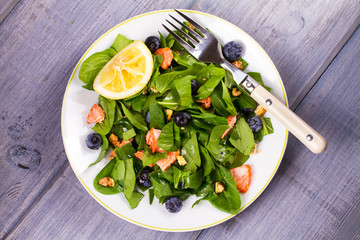 Spinach, salmon, blueberries and walnuts salad on white plate. View from above, top studio shot