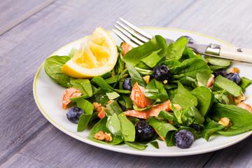 Spinach, salmon, blueberries and walnuts salad on white plate