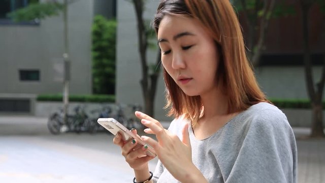 Young asian women standing and using smart phone on street of city and looking at camera smiling 