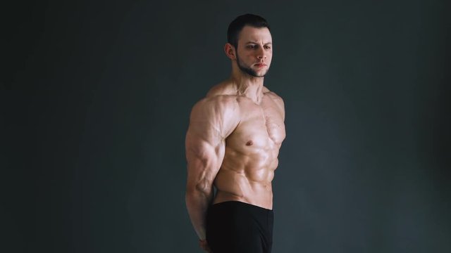 bodybuilder flexing his muscles at studio, dark grey background