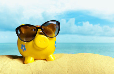Summer piggy bank with sunglasses on the beach