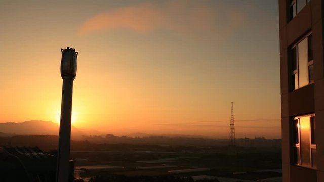 Time lapse of Sun rising behind chimney of factory and reflective image of sunrise on window surface 
