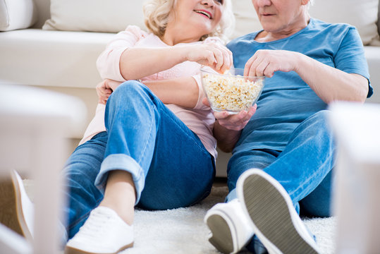 Cropped shot of happy senior couple eating popcorn on sofa