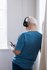 Back view of senior man in black headphones using smartphone