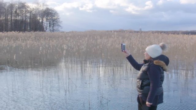 Woman taking pictures or video on a lake shore