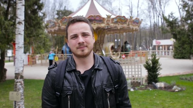 Portrait of a young man in a park on the background of a carousel